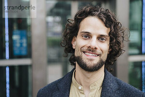 Happy young businessman with curly hair outside building