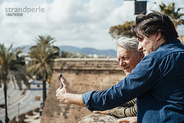 Glücklicher älterer Mann mit Sohn  der an einem sonnigen Tag ein Selfie per Smartphone macht