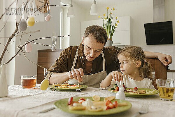 Vater und Tochter essen zu Hause Pfannkuchen zum Frühstück