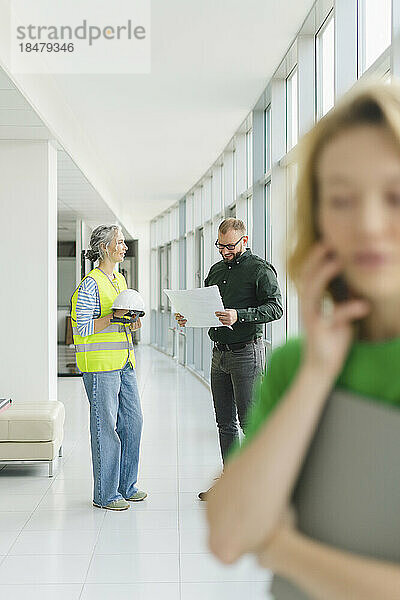 Businessman meeting with engineer on office floor with woman on the phone in foreground