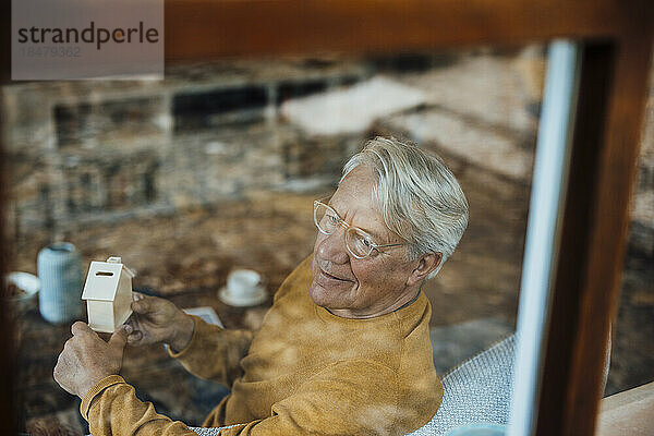 Lächelnder älterer Mann mit Musterhaus durch Fenster gesehen
