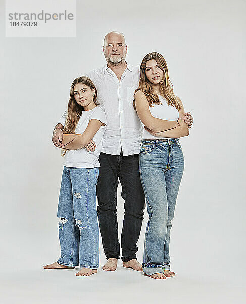 Daughter with arms crossed standing by father against white background