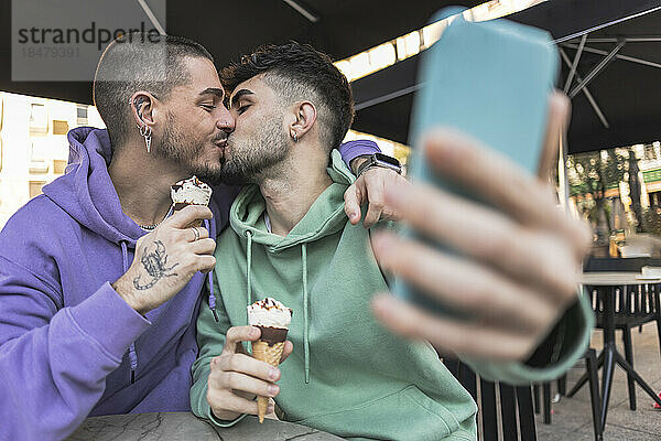Gay couple kissing and taking selfie over mobile phone at cafe