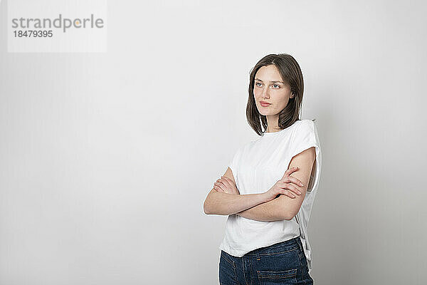 Contemplative woman standing with arms crossed against white background