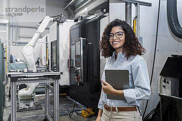 Glücklicher junger Ingenieur  der mit Tablet-PC vor der Maschine steht