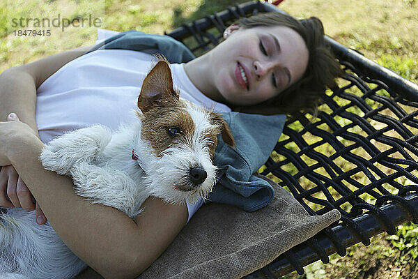 Junge Frau mit Jack Russell Terrier liegt auf Hängematte im Park