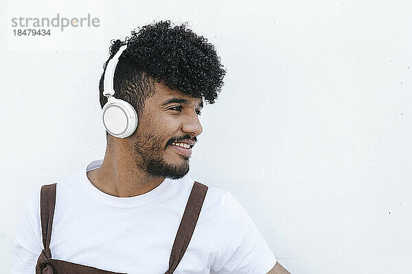 Happy young man wearing headphones listening to music in front of wall