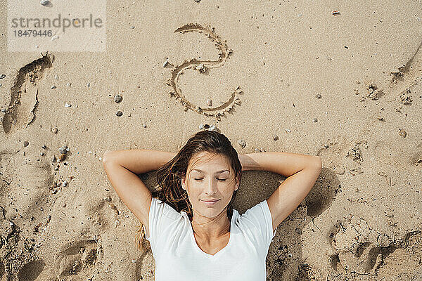 Frau mit geschlossenen Augen schläft im Sand am Strand