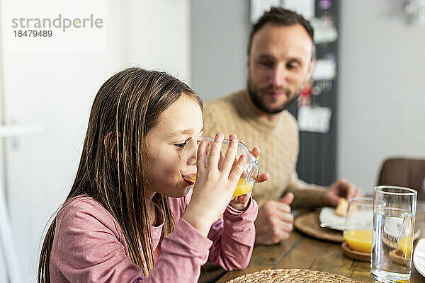 Girl drinking juice with father having breakfast at home