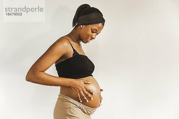 Glückliche schwangere Frau berührt Bauch vor weißer Wand