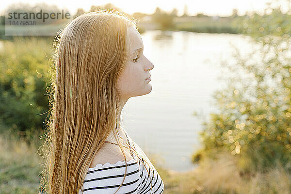Thoughtful girl with blond hair in front of lake