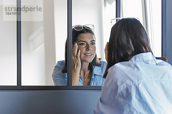 Woman touching face looking in mirror at home