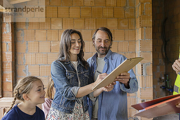 Glückliche Familie mit Frau  die auf der Baustelle eine Vereinbarung unterzeichnet