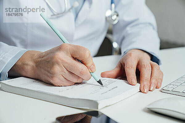 Arzt schreibt Rezept mit Stift am Schreibtisch