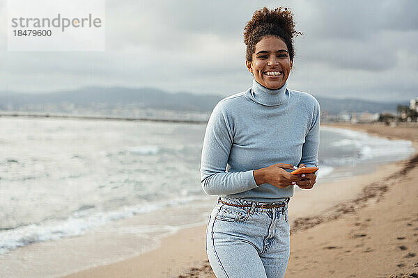 Glückliche junge Frau mit Smartphone am Strand