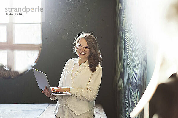 Happy businesswoman standing with laptop