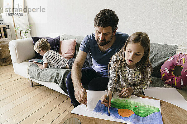 Father painting with daughter sitting on sofa at home