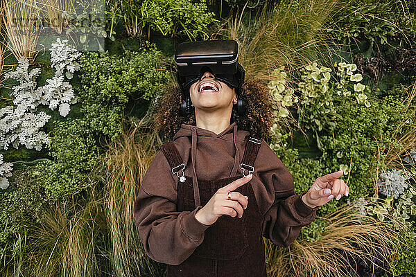 Glückliche Frau schaut durch eine VR-Brille vor Pflanzen zu