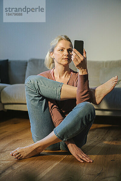 Reife Frau mit Mobiltelefon praktiziert zu Hause Yoga