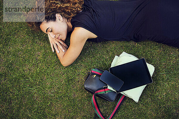 Lächelnde Geschäftsfrau liegt neben Bürokram im Gras im Park