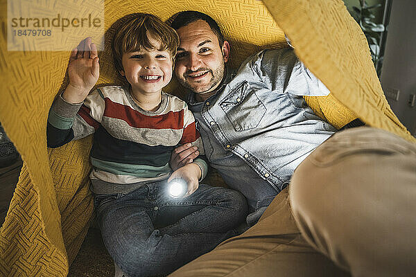 Happy father and son with torch under yellow blanket