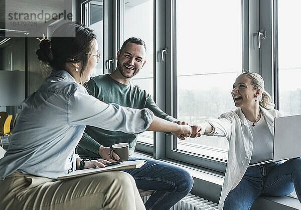 Fröhliche Geschäftskollegen geben sich im Büro gegenseitig Faustschläge