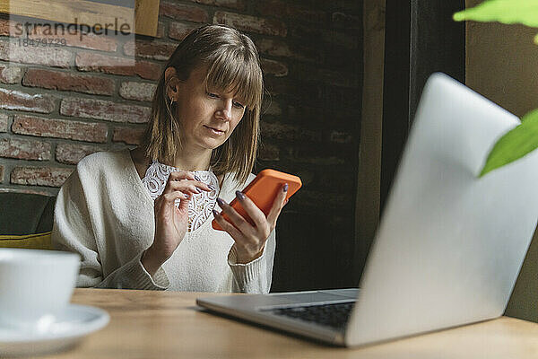 Freiberufler nutzt Smartphone und Laptop am Tisch im Café