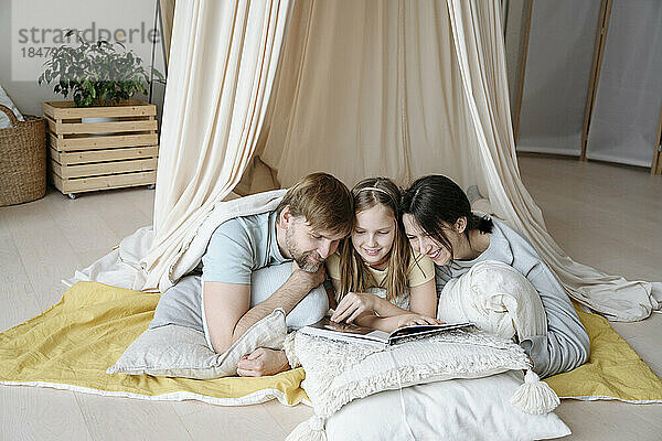 Glückliche Mutter  Vater und Tochter lesen Buch im Zelt zu Hause