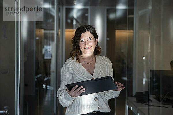 Lächelnde Geschäftsfrau mit Laptop im Flur am Arbeitsplatz