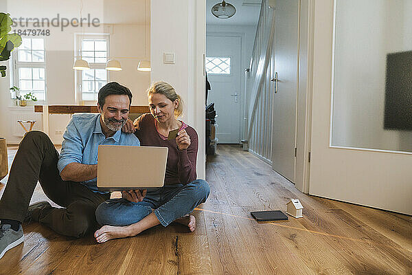 Mann und Frau erledigen Online-Einkäufe und sitzen zu Hause auf dem Boden
