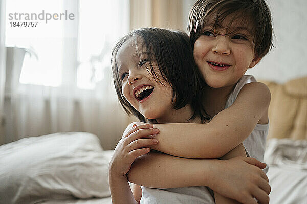 Glücklicher Junge umarmt Bruder im Schlafzimmer zu Hause