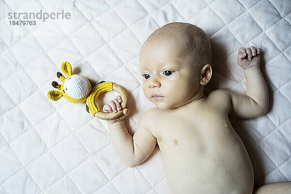 Shirtless baby boy with toy lying on bed at home