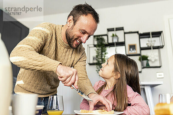 Glücklicher Vater serviert seiner Tochter am Tisch Frühstück