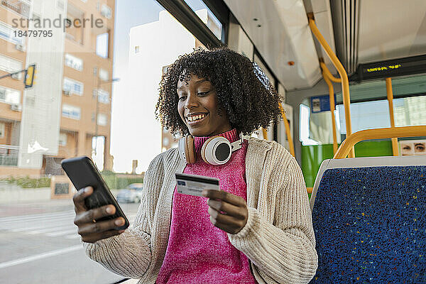 Glückliche Frau mit Kreditkarte und Smartphone in der Straßenbahn