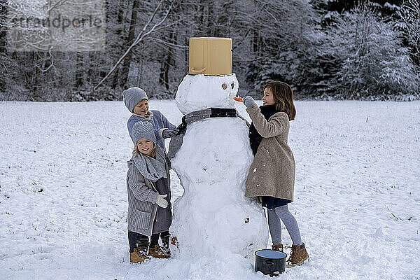 Bruder und Schwestern bauen Schneemann auf Schneefeld