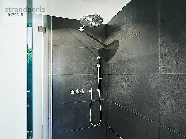 Shower amidst black tile wall in bathroom of modern apartment