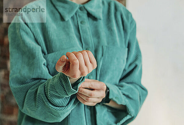 Frau knöpft Handgelenksknopf eines grünen Hemdes zu