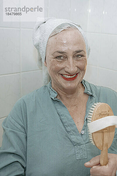 Glückliche ältere Frau hält Holzbürste im Badezimmer