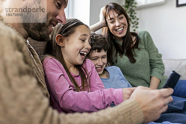 Glückliche Familie  die zu Hause ihr Mobiltelefon nutzt