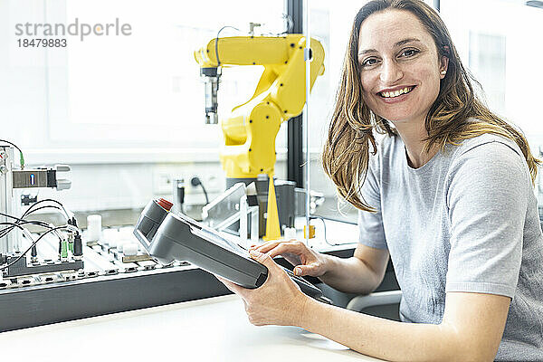 Facharbeiterin in Roboterfabrik steuert Roboterarm mit digitaler Steuerung