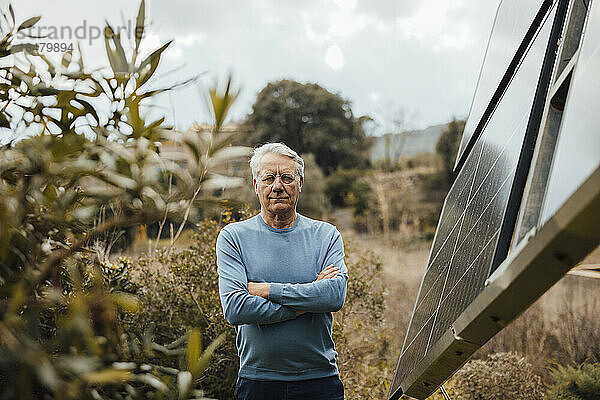 Älterer Mann mit verschränkten Armen steht neben Sonnenkollektoren