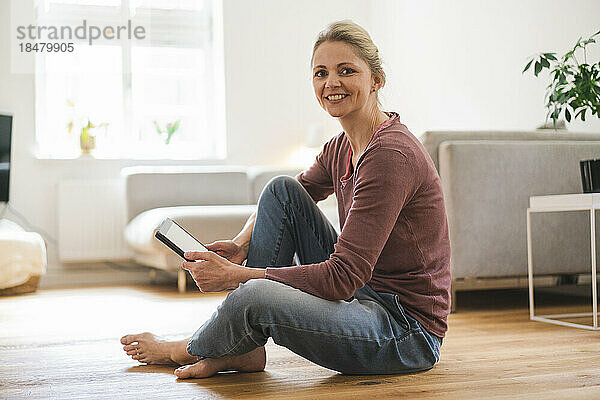 Glückliche Frau mit Tablet-PC sitzt zu Hause auf dem Boden