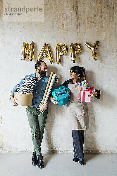 Happy couple holding gift boxes leaning on wall