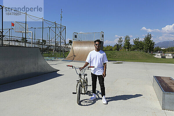 Junger Mann steht mit BMX-Fahrrad im Skatepark