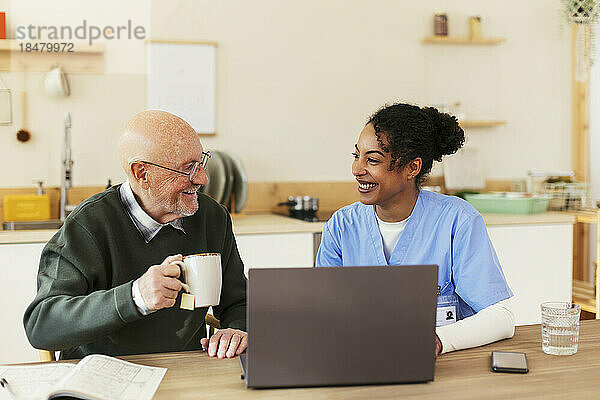 Glücklicher älterer Mann und Hausmeister  der zu Hause vor dem Laptop sitzt