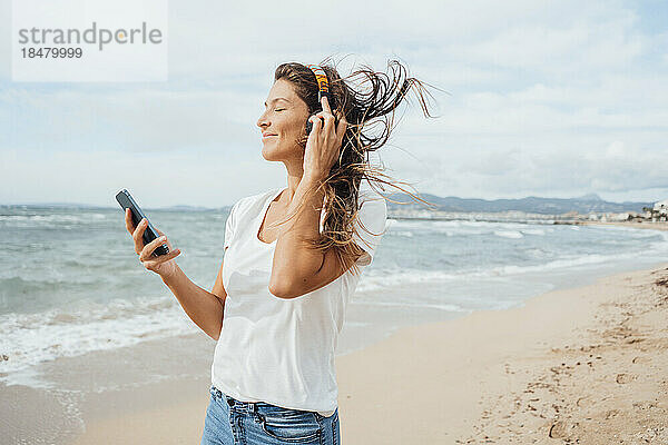 Lächelnde Frau genießt es  am Strand Musik über Kopfhörer zu hören