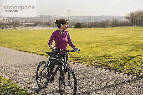Reife Frau steht an einem sonnigen Tag mit dem Fahrrad