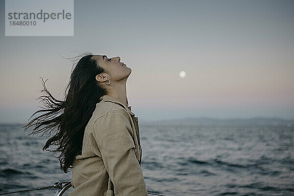 Frau mit geschlossenen Augen am Meer bei Sonnenuntergang