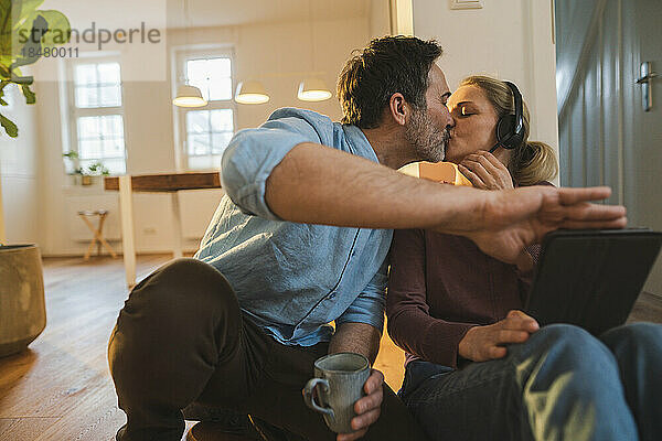 Zärtlicher Ehemann küsst Ehefrau mit Headset im Heimbüro