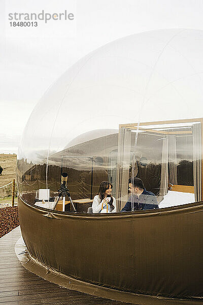 Young couple having coffee sitting inside dome hotel